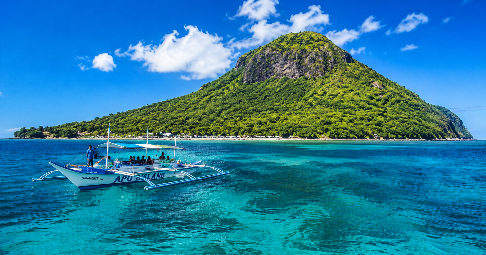 Apo Island day trip from Dumaguete Philippines — bangka outrigger boat on turquoise water approaching the volcanic island with coral reef visible below