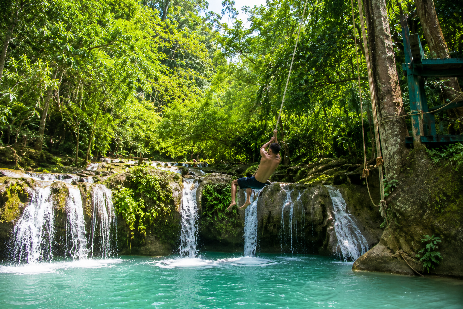 Person on rope swing at Cambugahay Falls Siquijor mid-air above turquoise pool — the most thrilling activity on the island