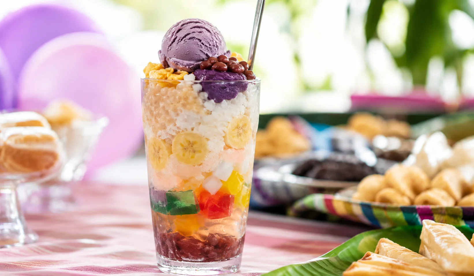 Halo-halo Filipino birthday dessert — tall glass of shaved ice layered with ube halaya, sago pearls, nata de coco, red beans, and a scoop of ube ice cream on top