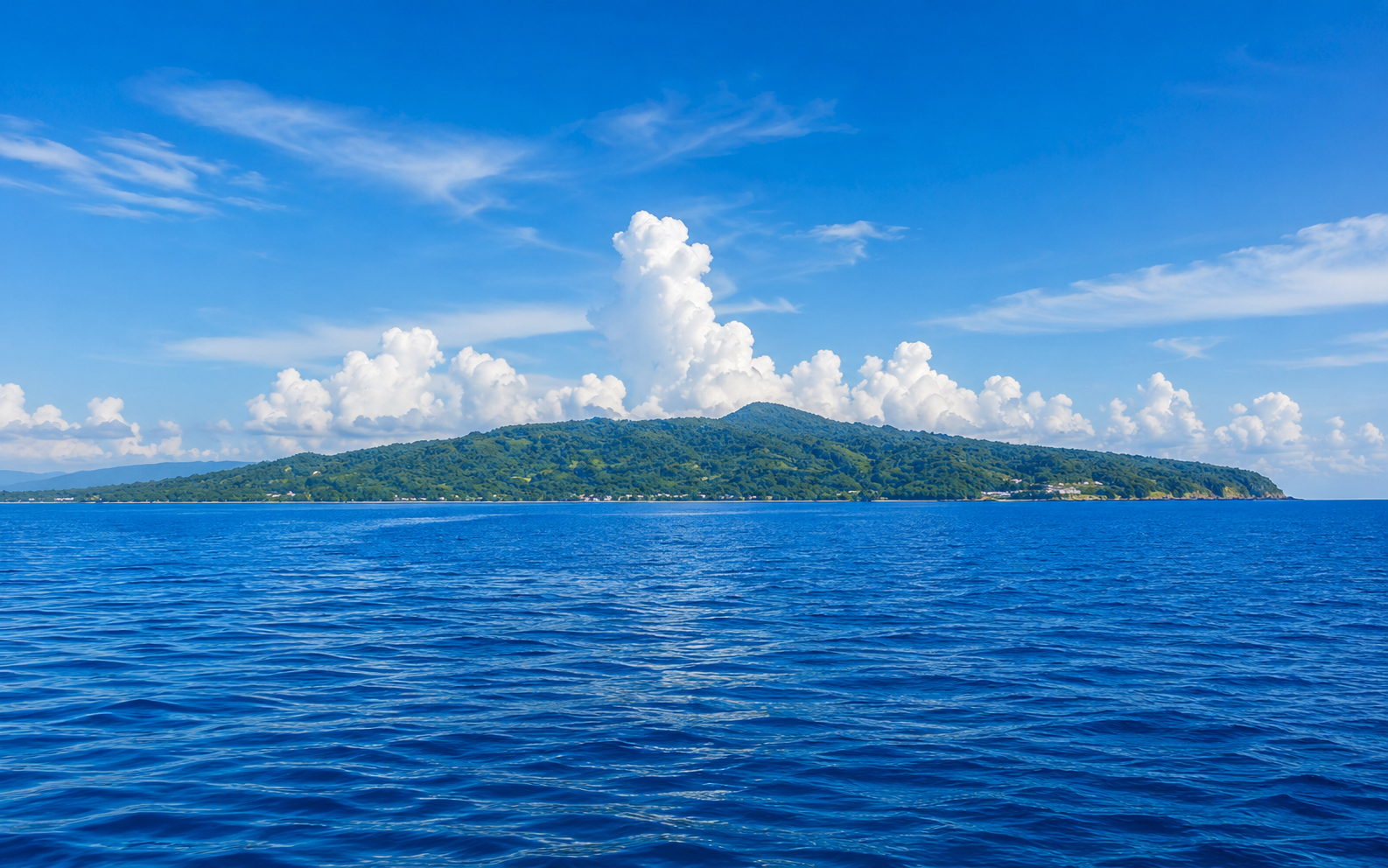 Siquijor island seen from the sea on approach — blue water in the foreground with the island's lush green hills on the horizon, Philippines