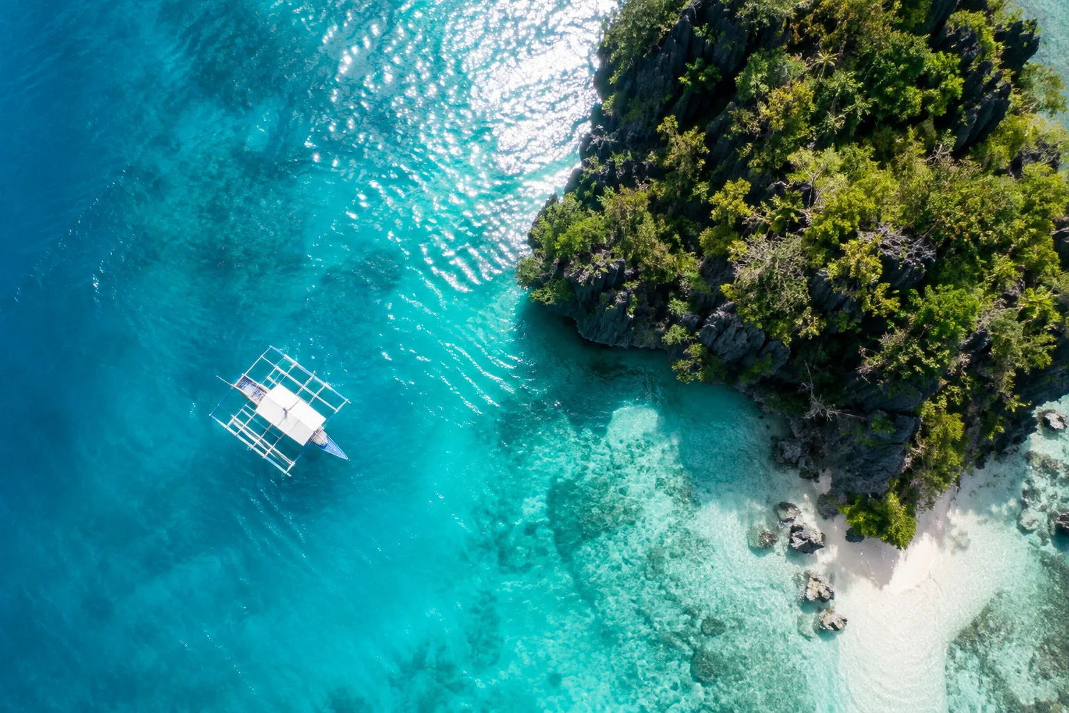 Aerial view of a traditional Filipino banca boat on turquoise water beside a tropical island